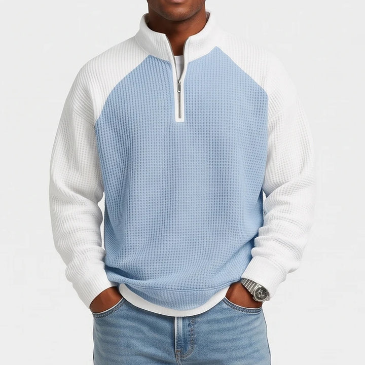 Man wearing a loose-fit, light blue and white waffle knit quarter-zip sweatshirt with raglan sleeves and jeans.