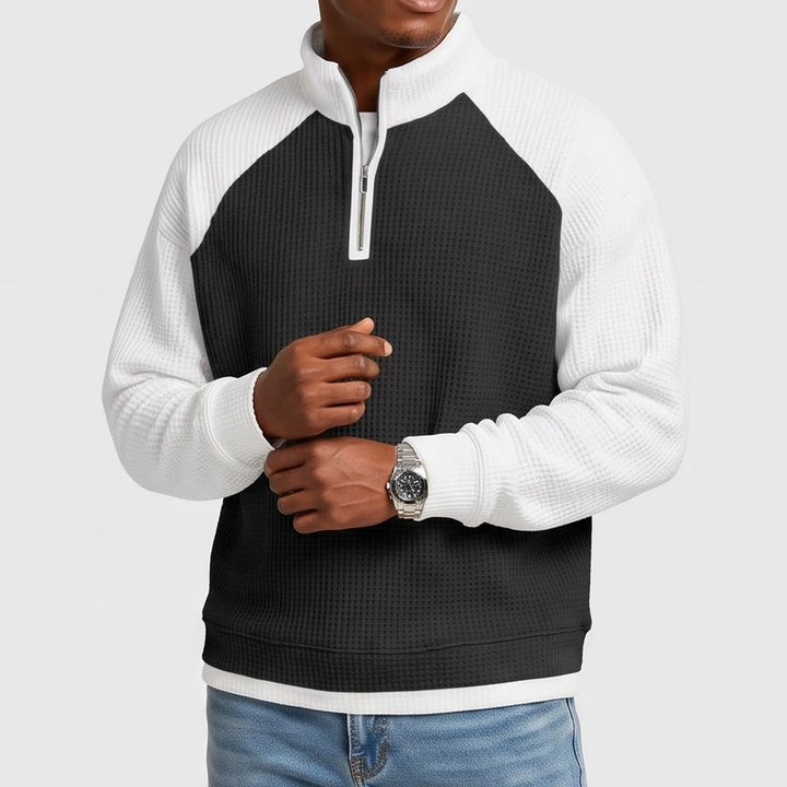 Man wearing a black and white color-block waffle knit quarter-zip sweatshirt with raglan sleeves and a silver watch.