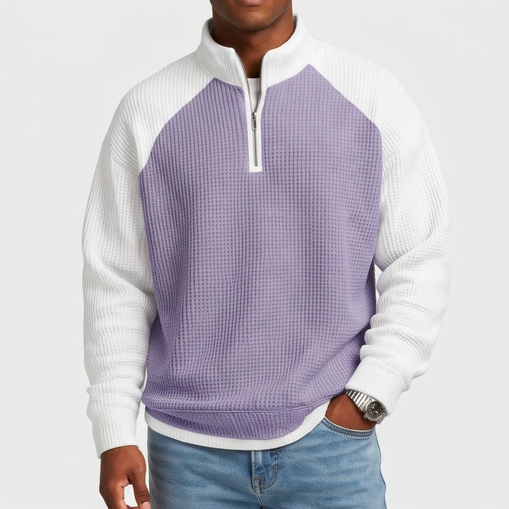 Man wearing a purple and white waffle-knit quarter-zip sweatshirt with raglan sleeves and light wash jeans.
