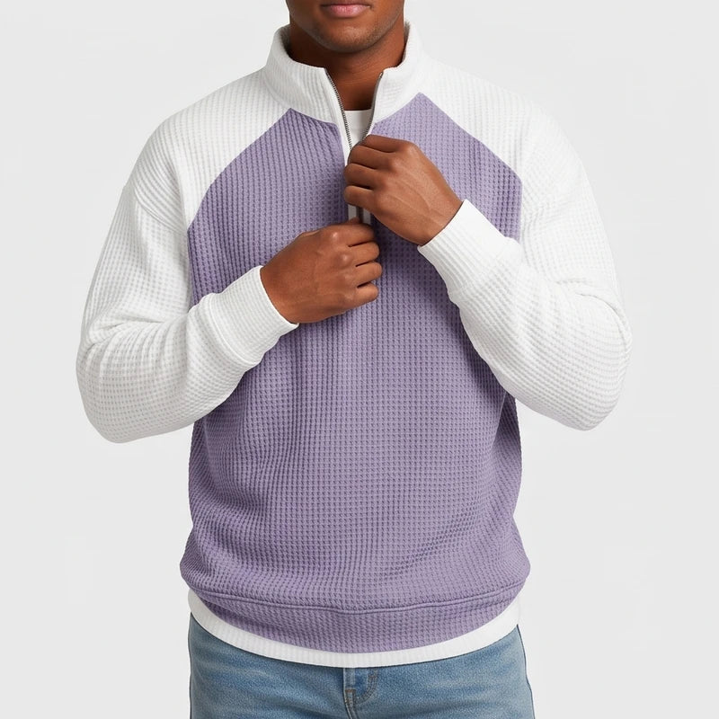 Man adjusting the zipper of a color block quarter-zip waffle knit sweatshirt, light purple body with white raglan sleeves.