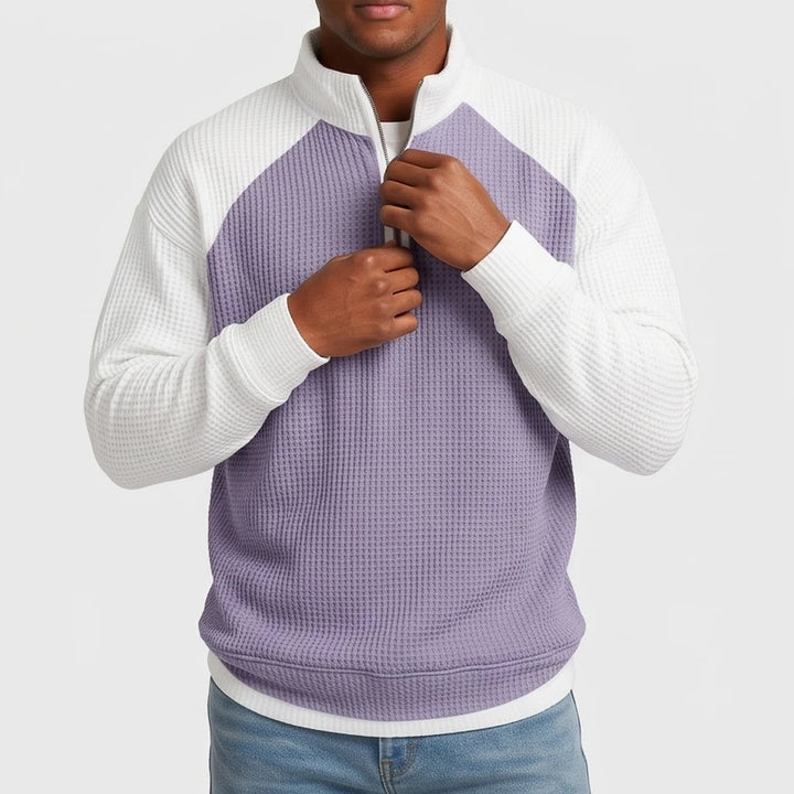 Man adjusting the zipper of a color block quarter-zip waffle knit sweatshirt, light purple body with white raglan sleeves.