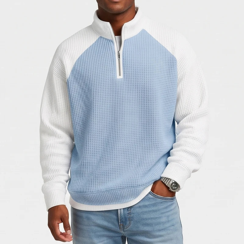 Man wearing a two-tone quarter-zip sweatshirt in blue and white waffle knit with light blue jeans.