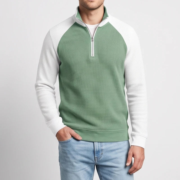 Man wearing a two-tone waffle knit quarter-zip sweatshirt with a sage green body and white raglan sleeves.