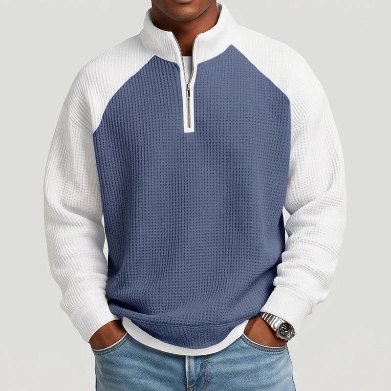 Man wearing a blue and white color-block waffle knit quarter-zip sweatshirt with raglan sleeves and light wash jeans.
