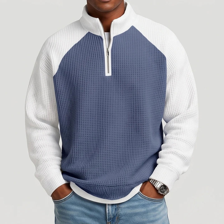 Man wearing a blue and white color-block waffle knit quarter-zip sweatshirt with raglan sleeves and light wash jeans.