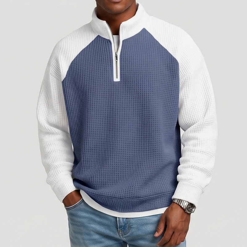Man wearing a two-tone blue and white waffle knit quarter-zip sweatshirt, hands in pockets, against a plain white background.