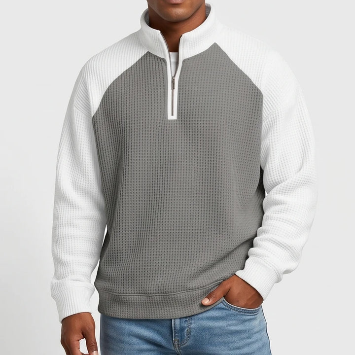 Man wearing a grey and white waffle knit quarter-zip sweatshirt with raglan sleeves and a white zipper.