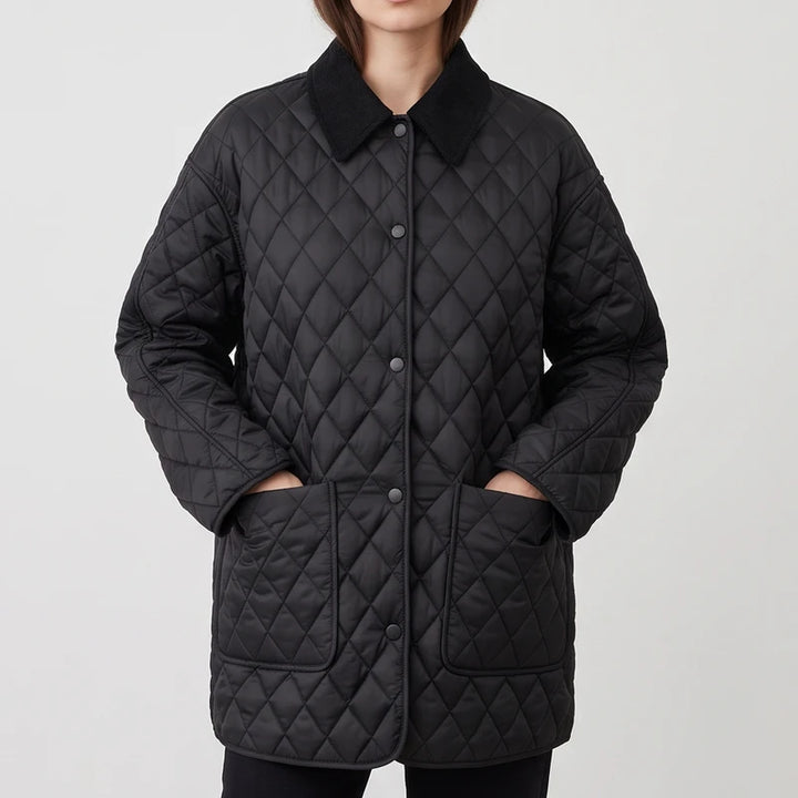 Woman wearing a black quilted jacket with a corduroy collar, button front closure, and hands in two large patch pockets.