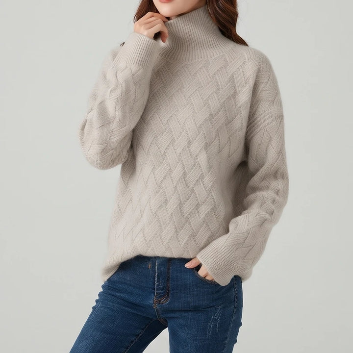 Woman wearing a beige textured mock neck knit sweater with a diagonal lattice pattern tucked into dark blue jeans.