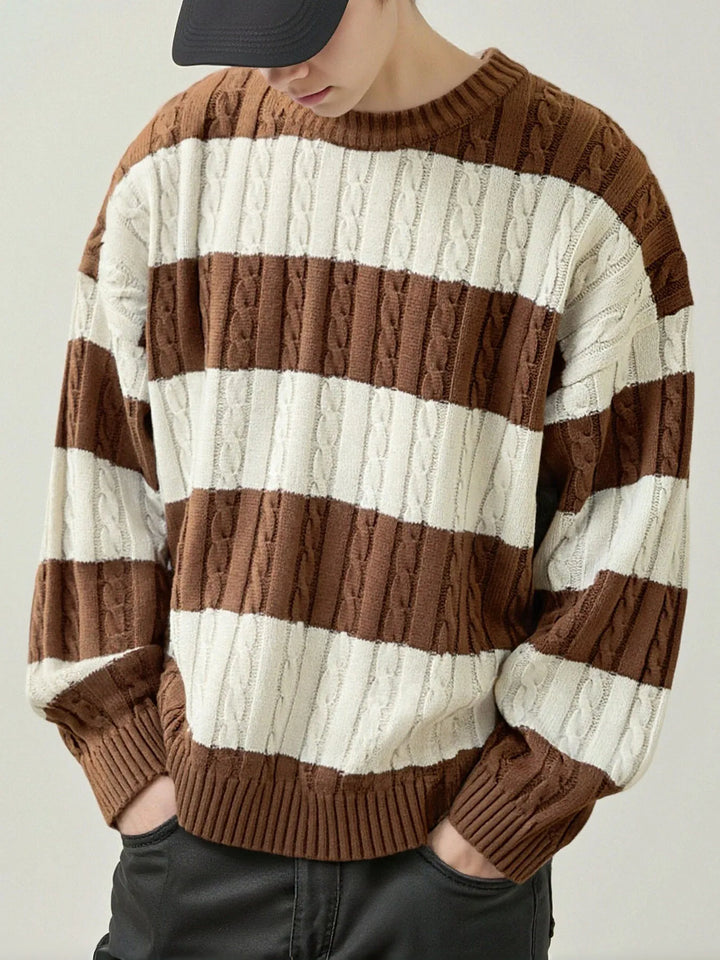Man wearing a brown and white striped cable knit sweater with ribbed cuffs and hem, hands in dark pants pockets.