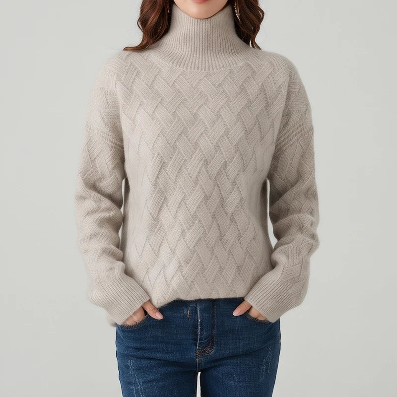 Woman wearing an oatmeal textured knit turtleneck sweater with hands tucked into her blue jeans against a neutral background.