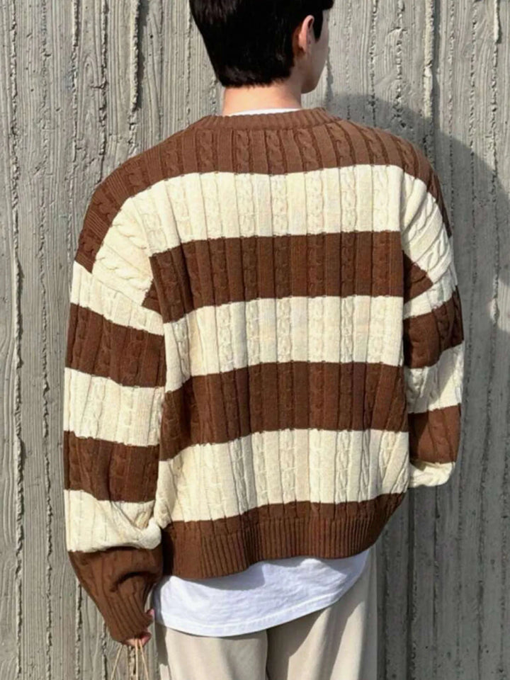Man wearing an oversized, cable knit sweater with alternating brown and cream horizontal stripes, seen from the back.