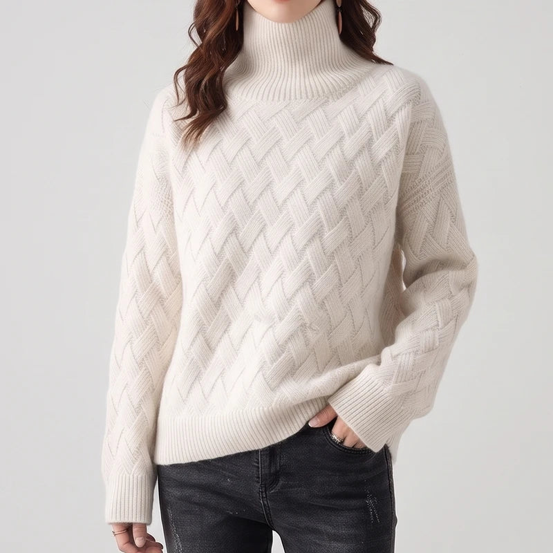 Woman wearing an off-white turtleneck sweater featuring a textured lattice knit pattern paired with dark wash jeans.