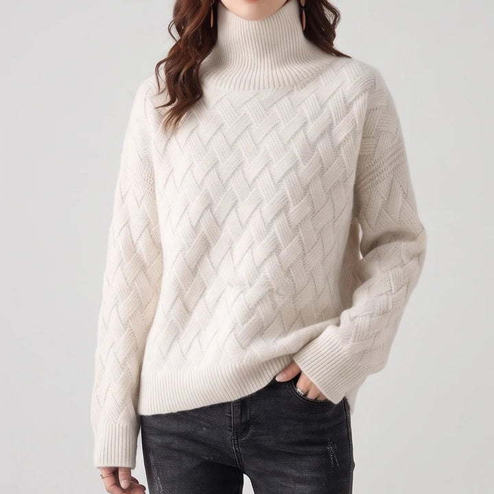 Woman wearing an off-white turtleneck sweater featuring a textured lattice knit pattern paired with dark wash jeans.