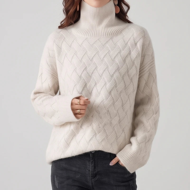 Woman wearing a cream-colored turtleneck sweater with a textured lattice knit pattern paired with dark denim jeans.