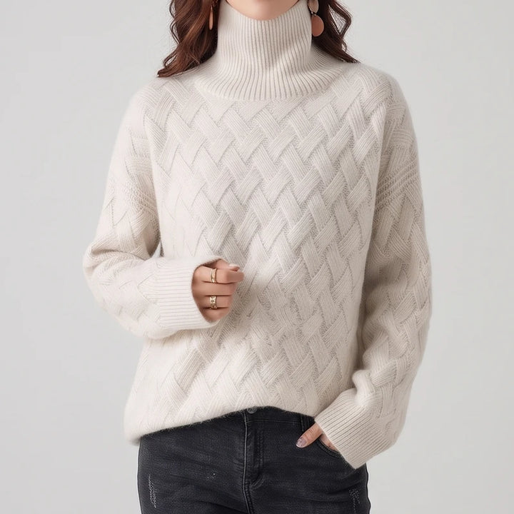 Woman wearing a cream-colored turtleneck sweater with a textured lattice knit pattern paired with dark denim jeans.