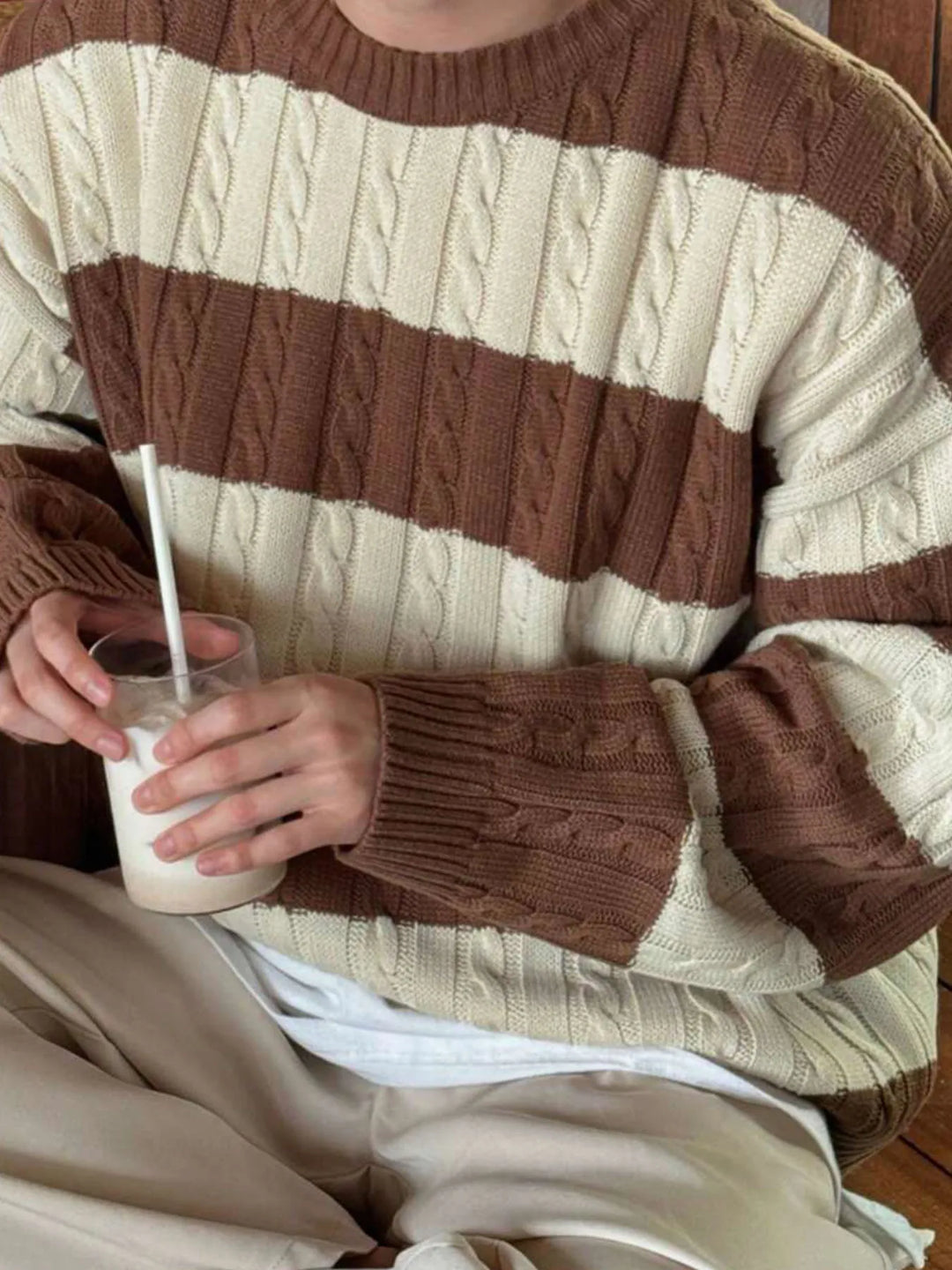 Person wearing a thick cable knit sweater with alternating wide cream and brown horizontal stripes.