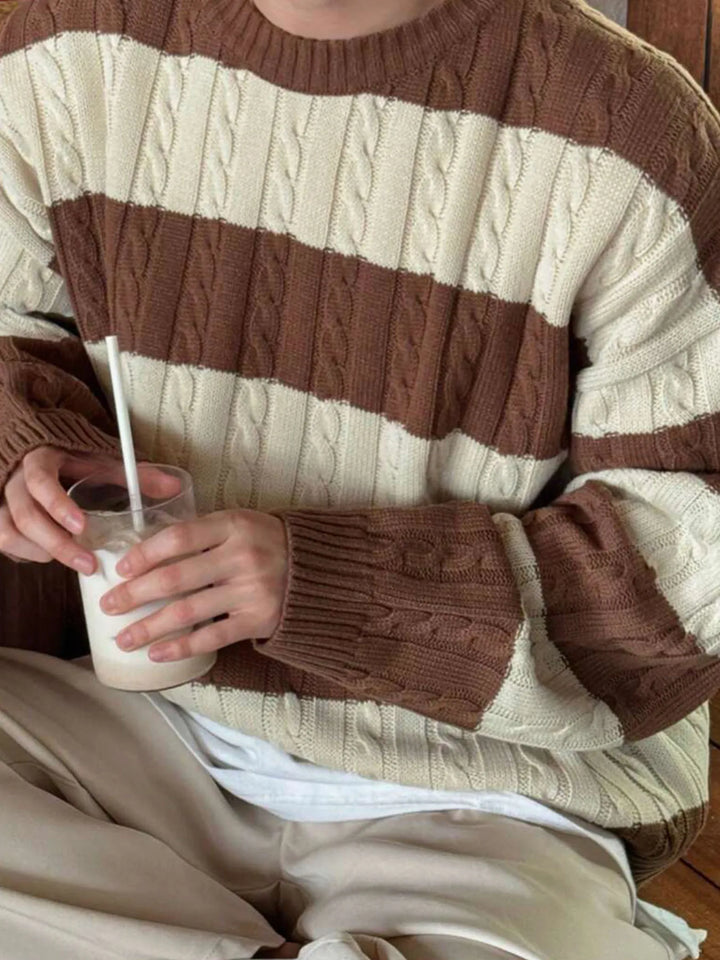 Person wearing a thick cable knit sweater with alternating wide cream and brown horizontal stripes.