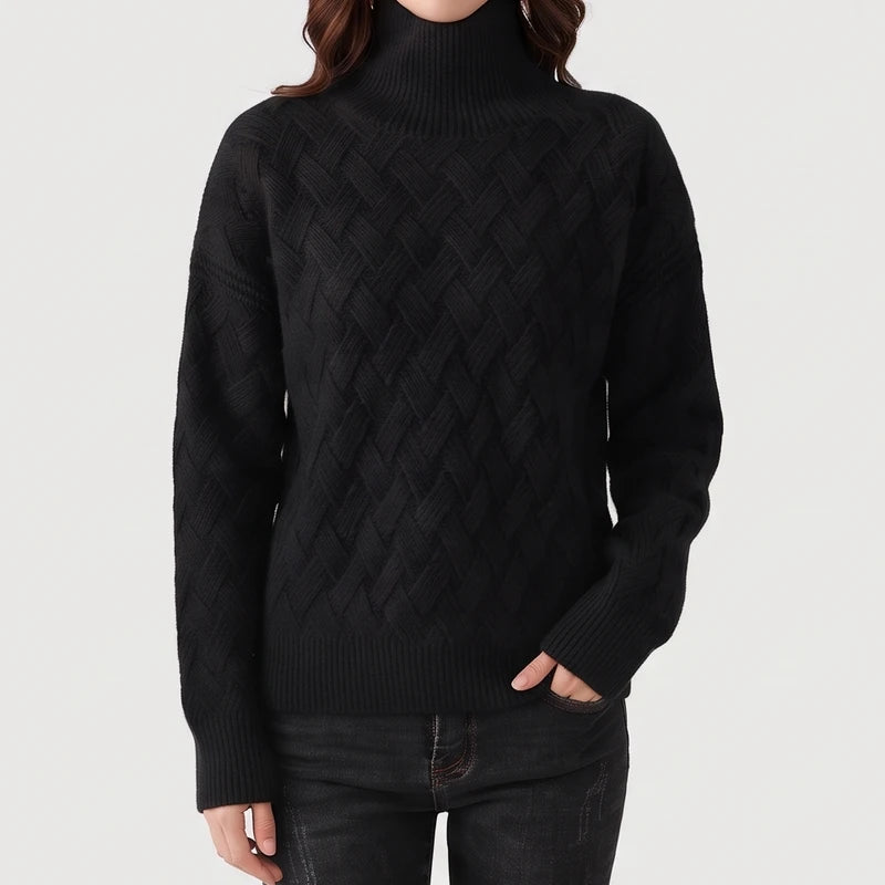 Woman wearing a black turtleneck sweater featuring a textured basketweave knit pattern, paired with dark jeans against a light background.