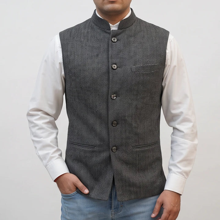 Man wearing a grey herringbone vest with a mandarin collar and front buttons over a white long-sleeve shirt.
