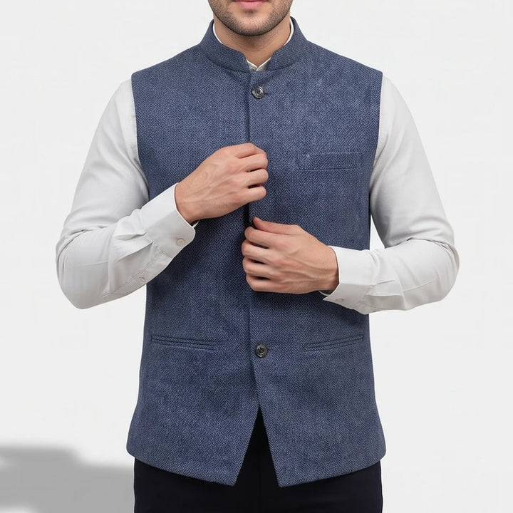 Man wearing a blue herringbone Nehru collar vest over a white dress shirt, adjusting the front buttons.