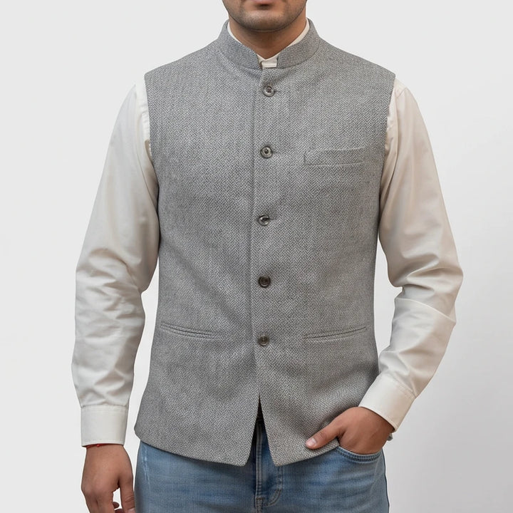 Man wearing a tailored light grey herringbone vest with a mandarin collar and buttons over a white dress shirt.