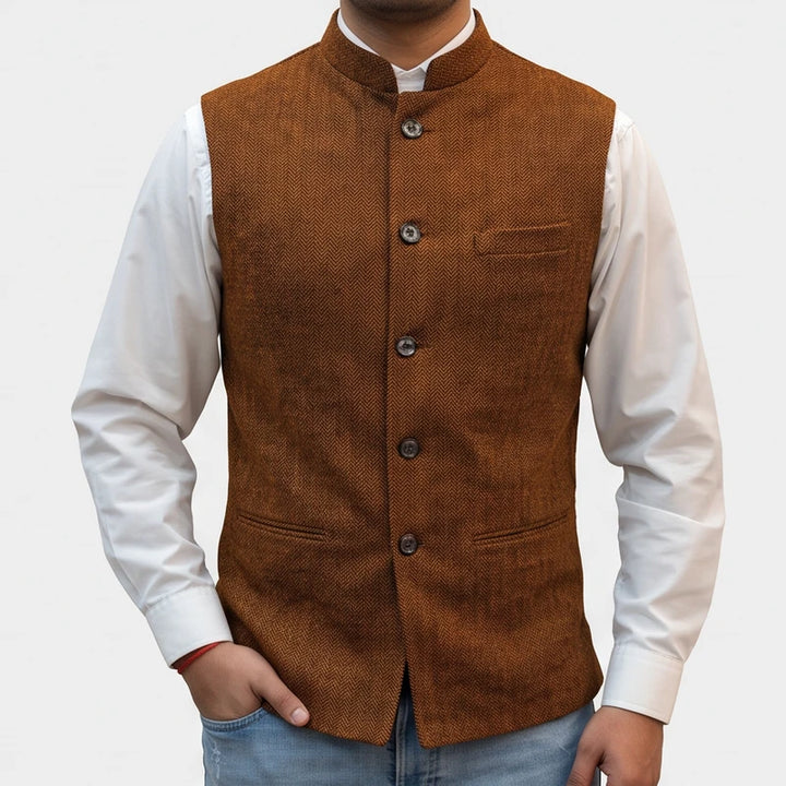 Man wearing a brown herringbone tweed vest with a mandarin collar over a crisp white dress shirt.