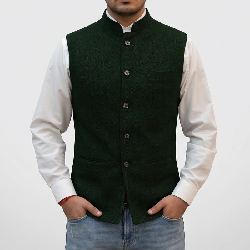 Man wearing a dark green button-front vest with a mandarin collar over a white shirt against a plain background.