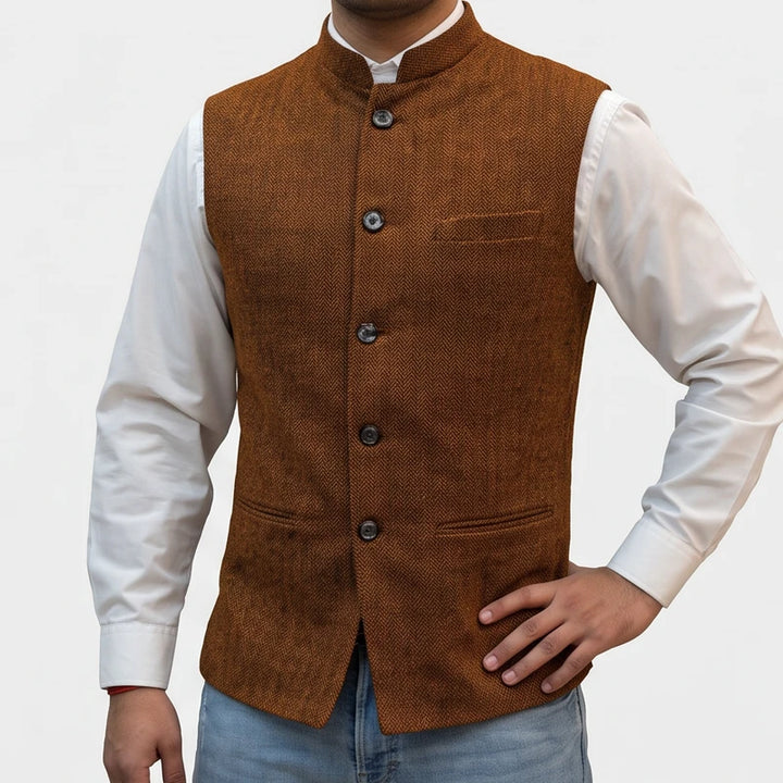 Man wearing a brown herringbone tweed vest with a mandarin collar over a white button-down shirt.