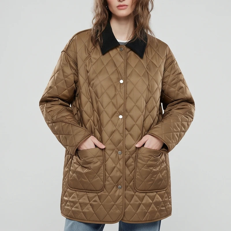 Woman wearing a long brown diamond-quilted jacket with a black collar and silver snap buttons, hands in patch pockets.