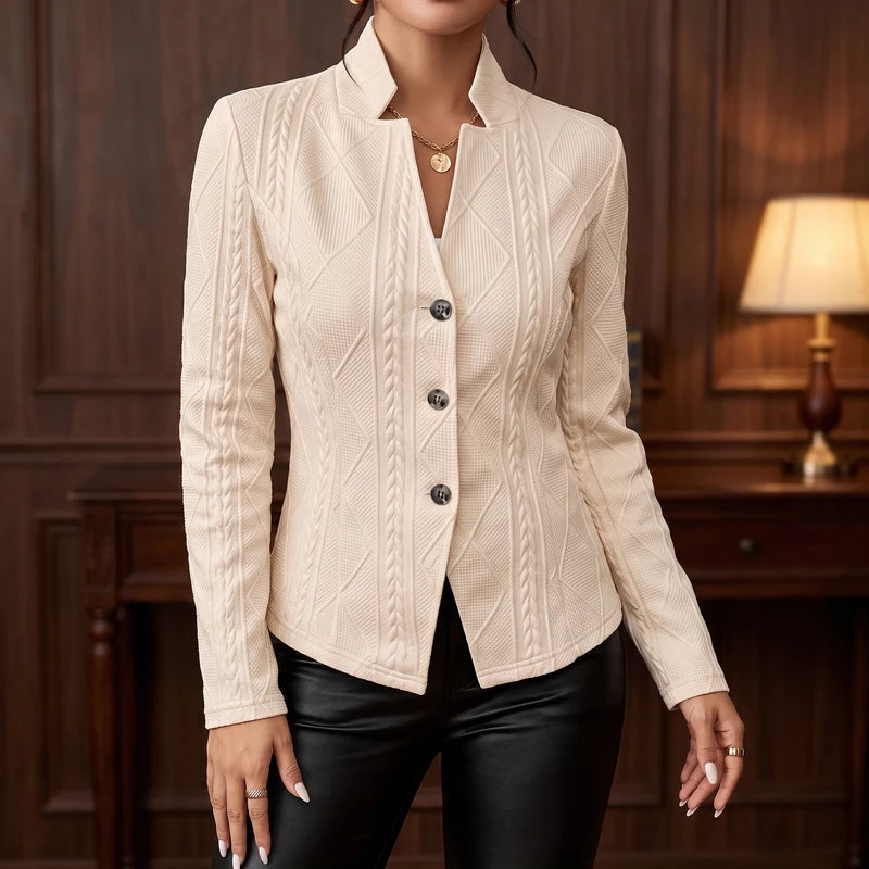 Woman wearing a cream textured blazer with cable and diamond patterns, a stand collar, and three dark buttons, over black pants.