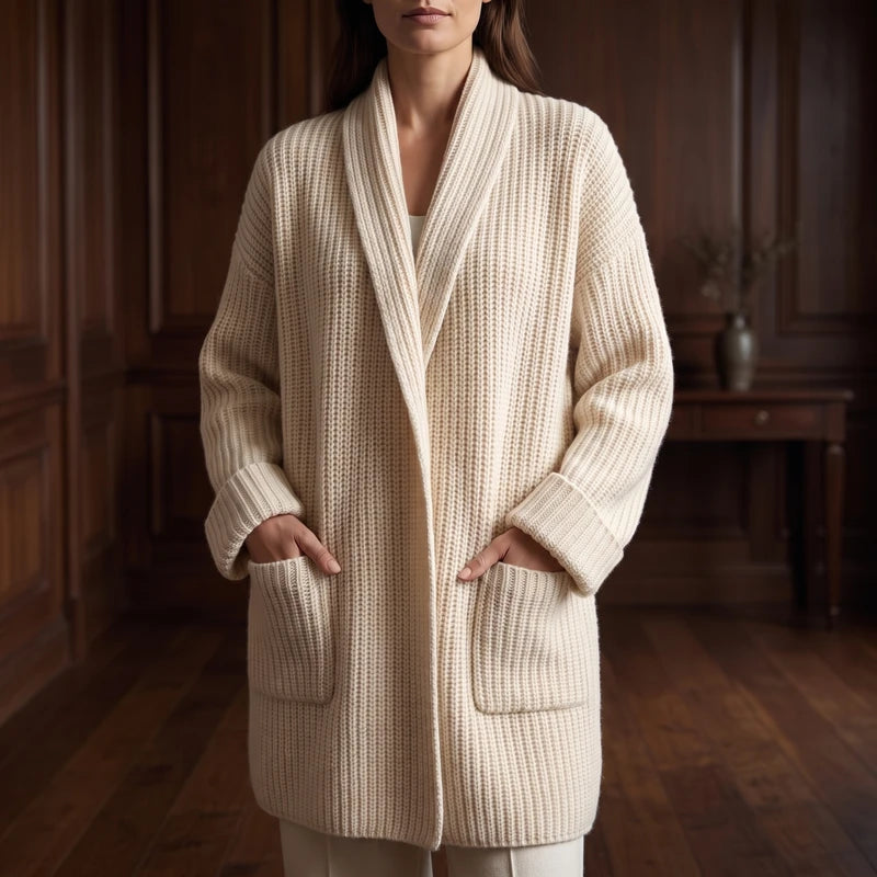Woman wearing a long, cream chunky knit cardigan with a wide shawl collar, cuffed sleeves, and large front pockets.
