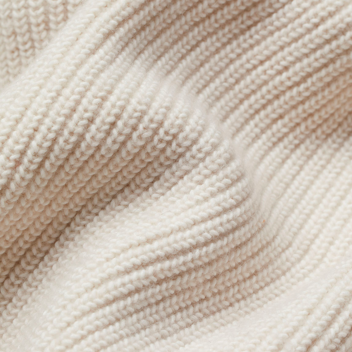 Close-up of a cream-colored chunky knit fabric with visible ribbed texture and soft folds.