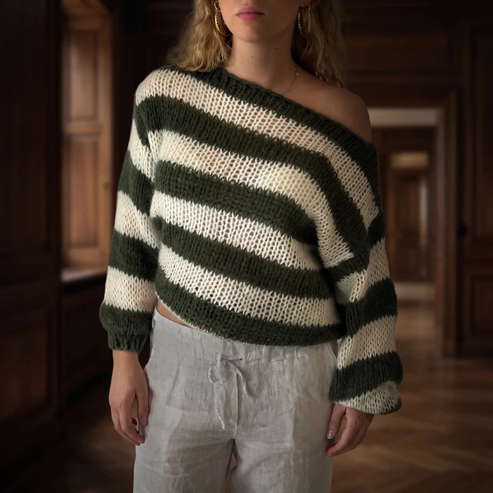 Woman wearing an off-the-shoulder, loose-knit oversized sweater with dark green and cream horizontal stripes, paired with light grey drawstring pants.