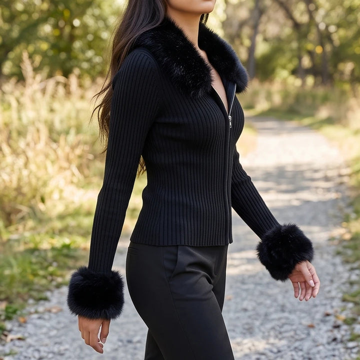 Woman wearing a black ribbed knit zip cardigan with a faux fur collar and cuffs, walking outdoors on a path.