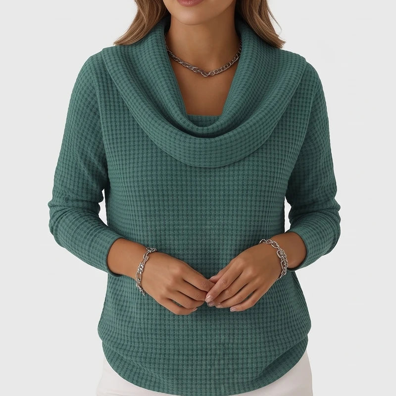 Woman wearing a teal waffle knit cowl neck sweater and silver chain jewelry, standing against a white background.