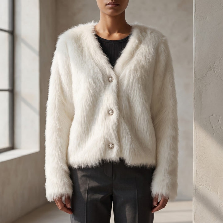 A model wearing a fluffy off-white faux fur cardigan with three large buttons, styled over a black top and dark gray trousers in a bright, modern loft setting.