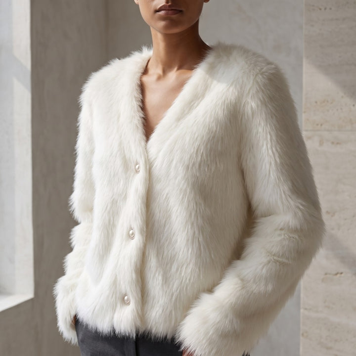 A model wearing a plush, off-white faux fur cardigan with a V-neck and decorative buttons, set against a neutral stone wall background.