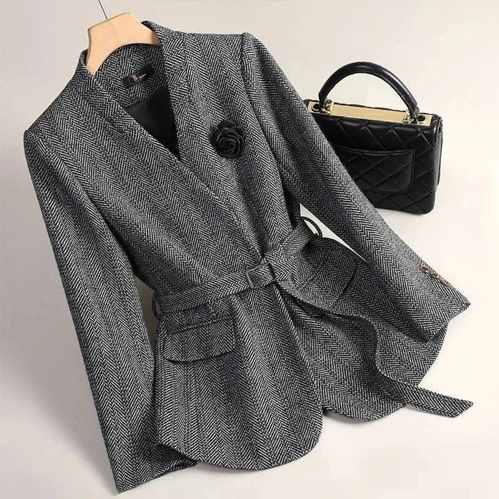 Gray and white herringbone blazer with a black rose lapel pin, belt, flap pockets, and a black quilted purse in background.
