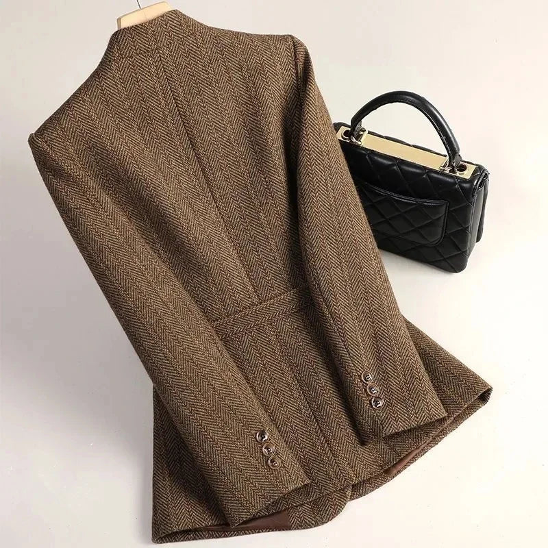 Brown herringbone blazer with three buttons on each cuff, displayed on a hanger next to a black quilted handbag.
