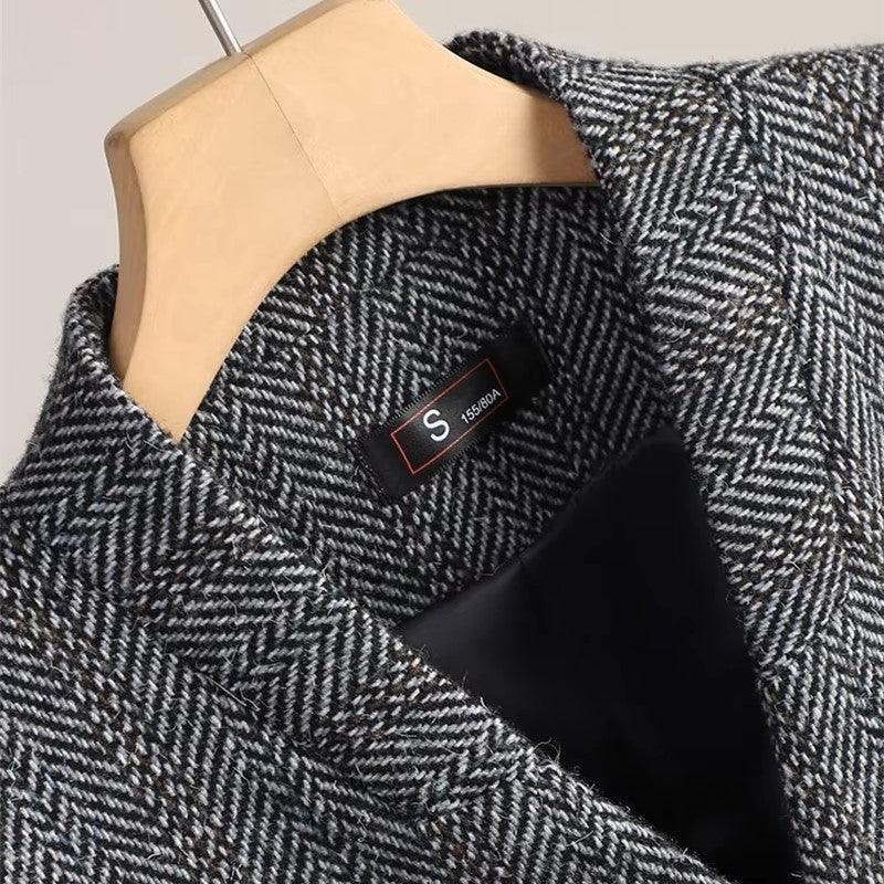 Close-up of a charcoal herringbone blazer with a black lining, hanging on a wooden hanger, displaying a size tag.