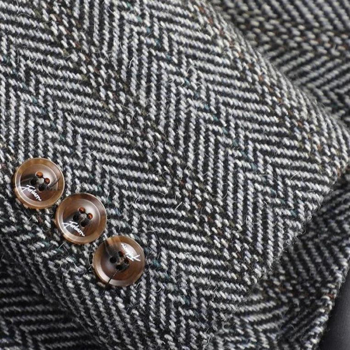 Close-up of a dark gray and white herringbone wool fabric sleeve with three brown buttons on the cuff.