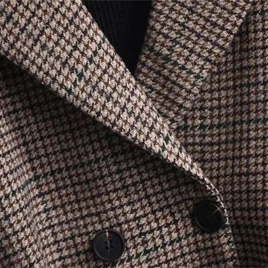 Close-up of a brown and tan houndstooth blazer with two dark buttons and a folded lapel over a black ribbed top.