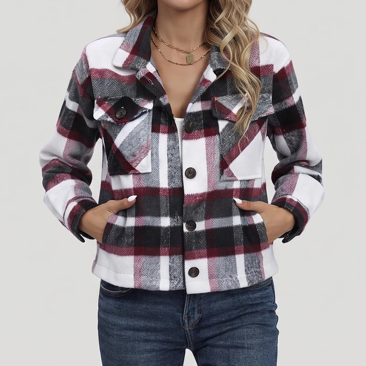 Woman wearing a red, white, and black plaid button-up shirt jacket with chest pockets and hands in side pockets.