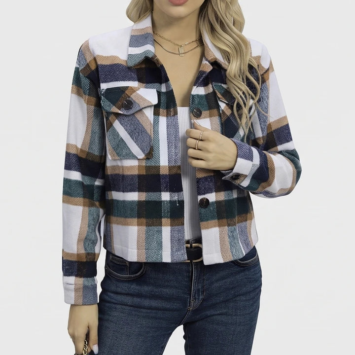 Woman wearing an open cropped plaid jacket in white, navy, green, and tan over a white top and blue jeans.