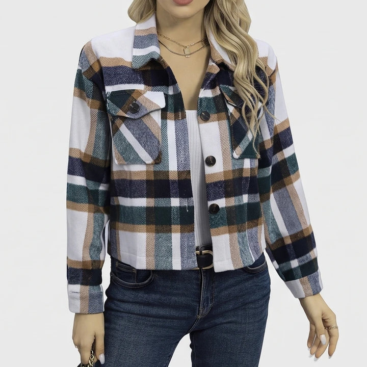 Woman wearing a cropped plaid shirt jacket in white, navy, brown, and green, over a white top and blue jeans.