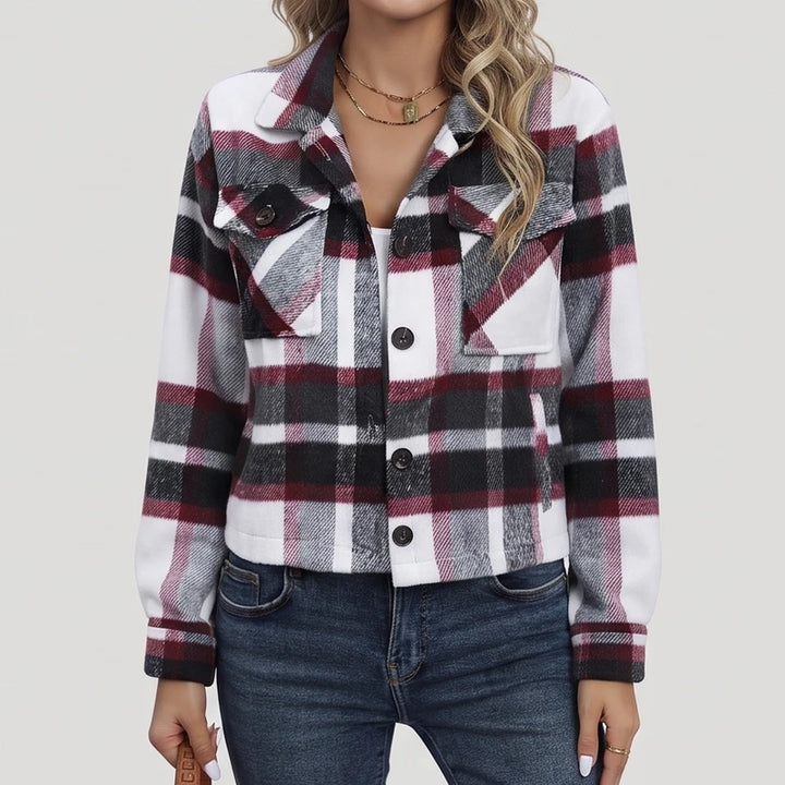 Woman wearing a black, white, and maroon plaid jacket with chest pockets and dark buttons, over a white top and blue jeans.