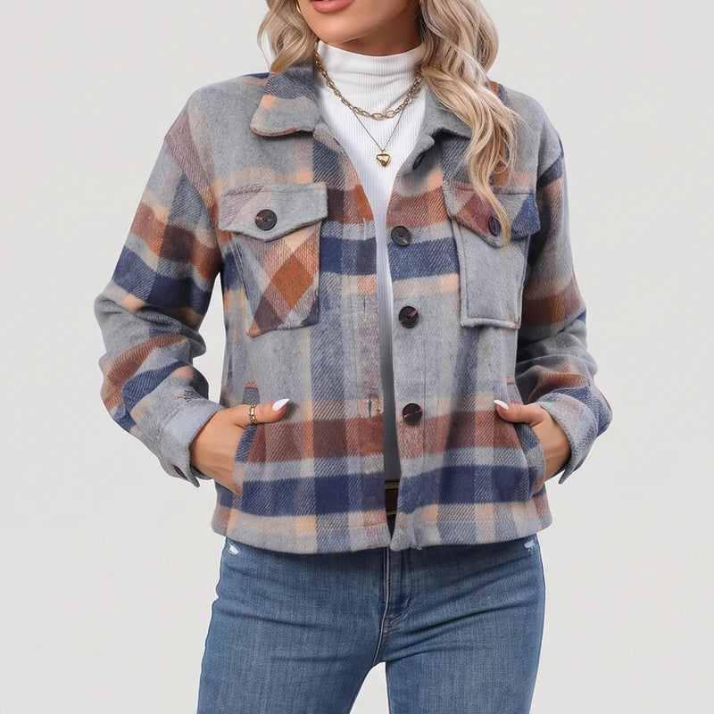 Woman wearing a gray, blue, and brown plaid jacket with two chest pockets, over a white turtleneck and blue jeans.
