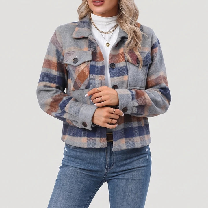 Woman wearing a light gray, blue, and brown plaid button-up jacket over a white turtleneck and blue jeans.