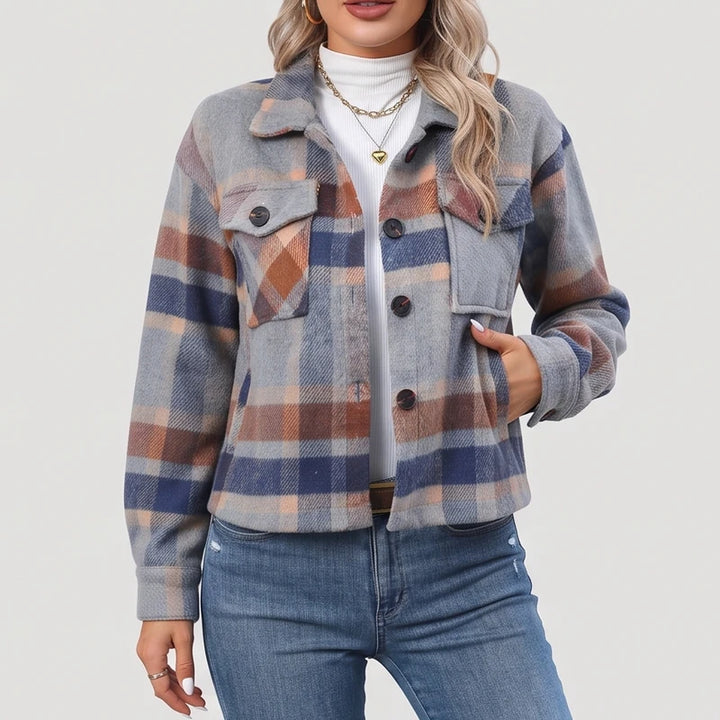 Woman wearing a gray, blue, and brown plaid jacket with chest pockets, dark buttons, and blue jeans.